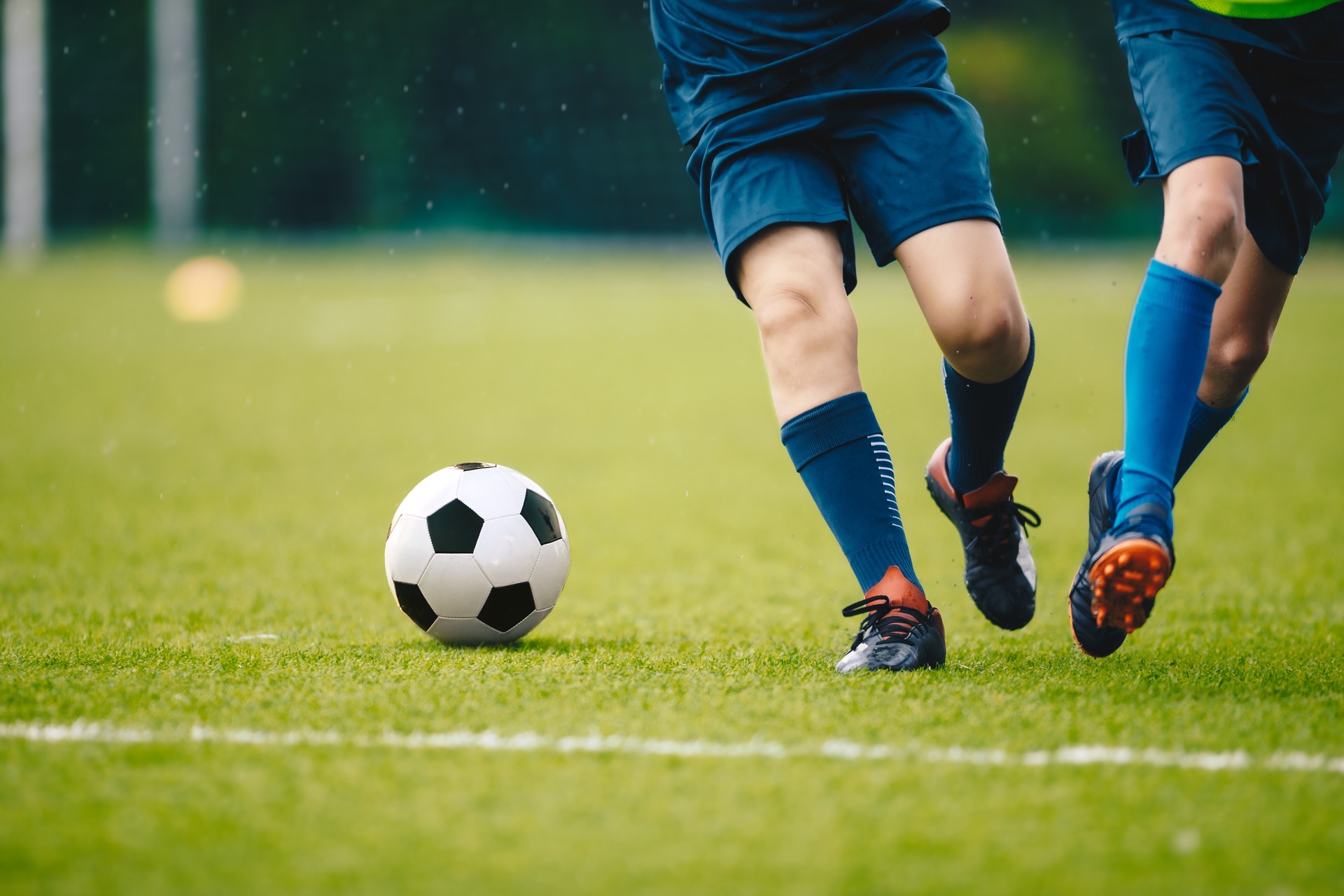 Two adult football players running and kicking a soccer ball. Legs of two young football players on a match. European football youth player legs in action